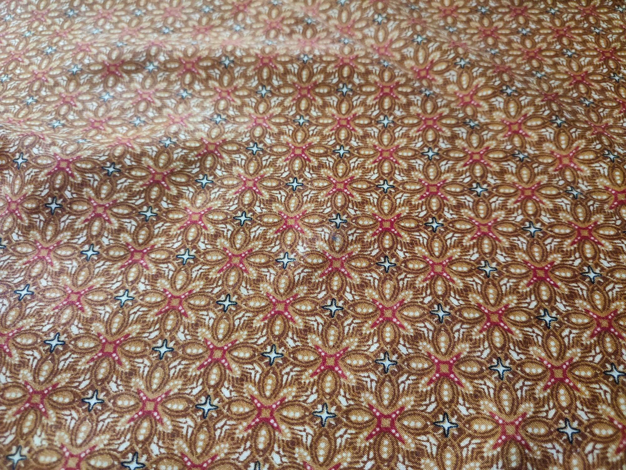 Close-up of a brown, red, and white traditional batik fabric with a repeating floral and geometric pattern.